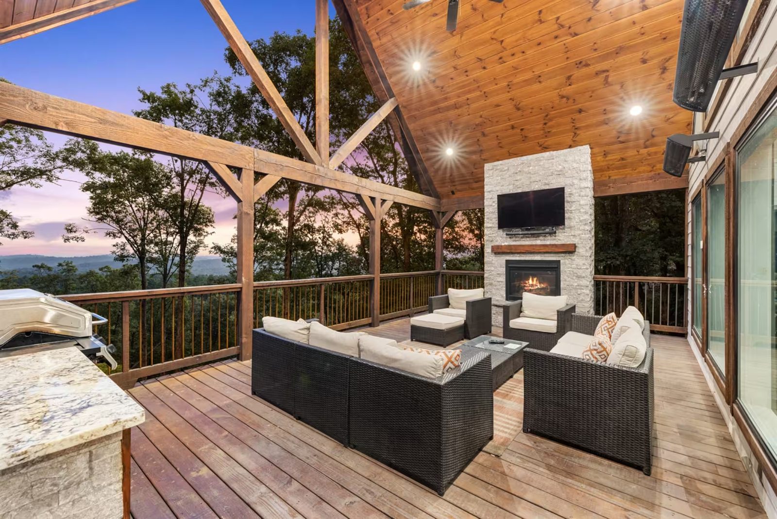 Covered deck with a stone fireplace, lounge seating, and sunset over the ridge.
